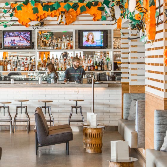 Two bartenders behind the bar at the Hive, with liquor bottles and tvs